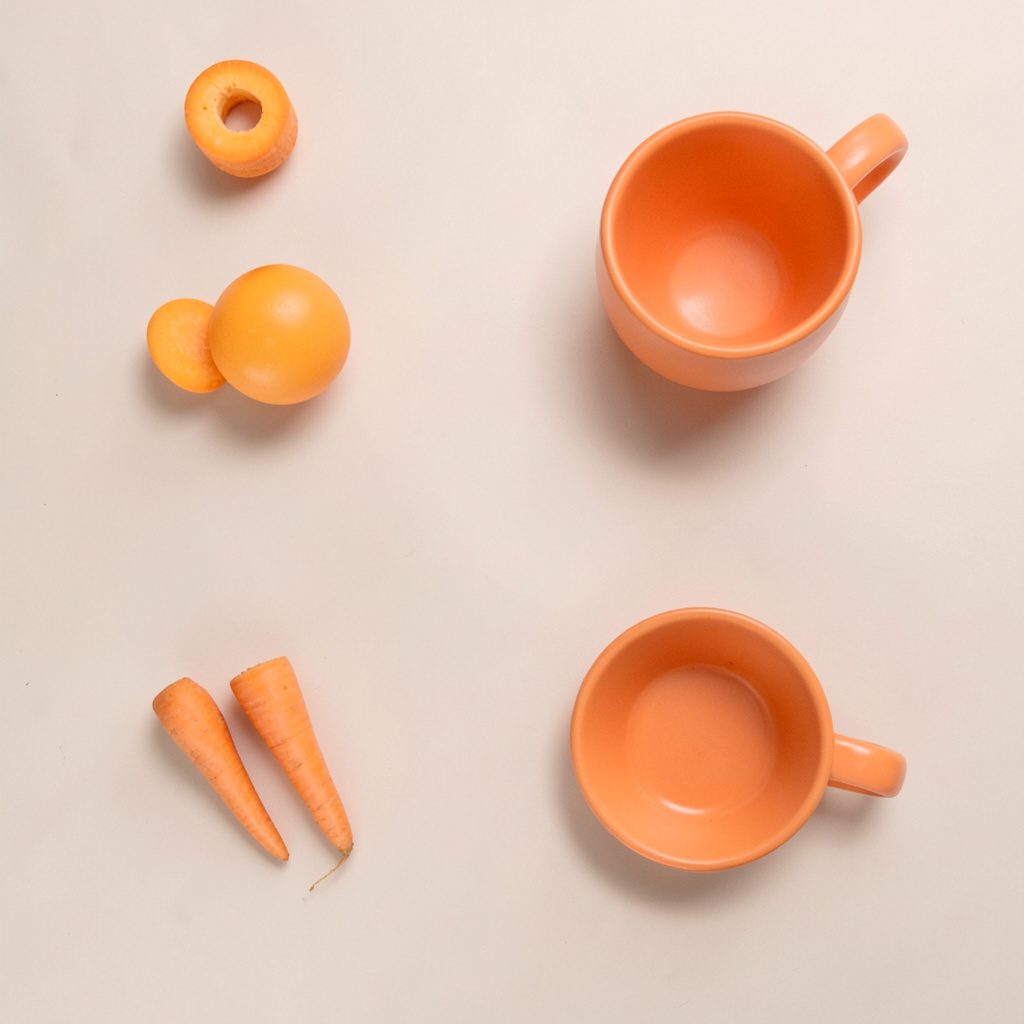 An overhead flat-lay photograph of an open hardcover book, a steaming ceramic mug, and scattered dried flower petals on a textured linen surface in soft neutral tones.
